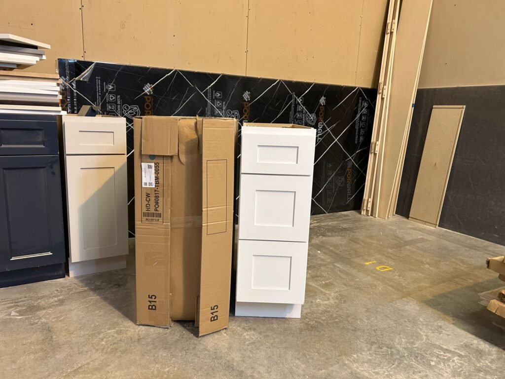 Flat-packed RTA cabinet box standing next to the same white shaker drawer base fully assembled